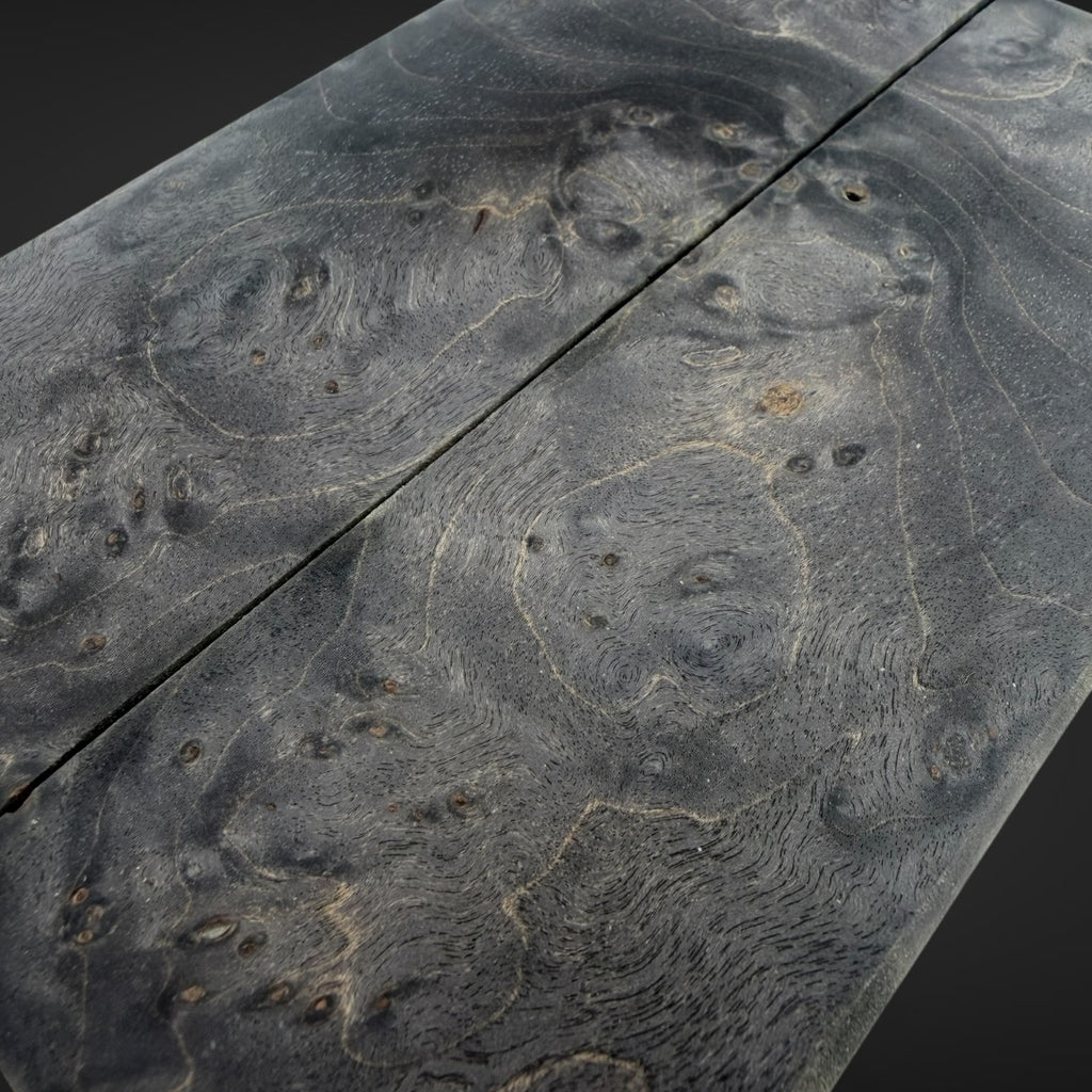 Close-up of a dark wood surface with dramatic swirling grain and burl-like patterns, showing natural wood texture and knots against a dark background.