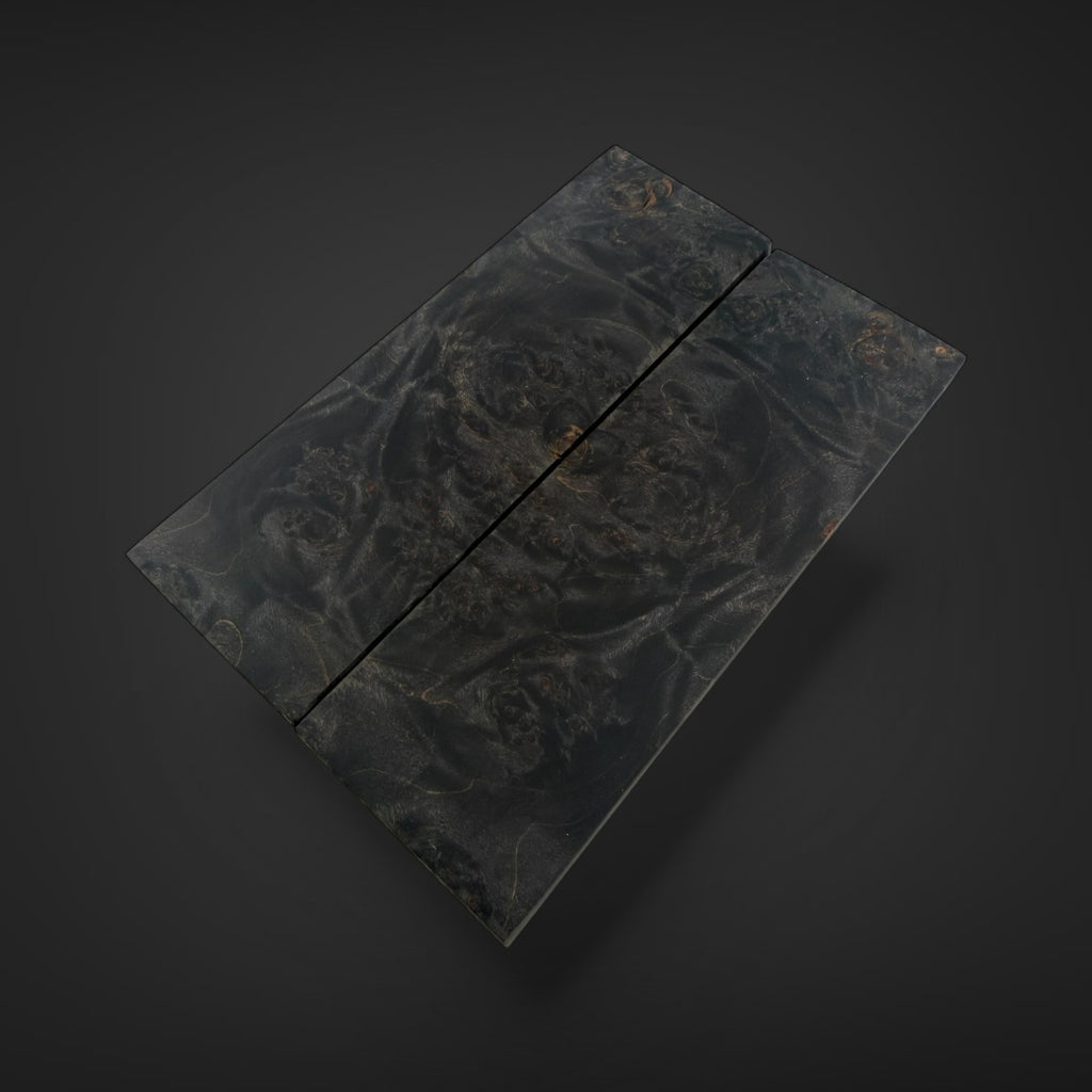 A rectangular black marble board with a natural swirling pattern and subtle gold flecks, shown on a dark gray background. Maple Burl knife scales 