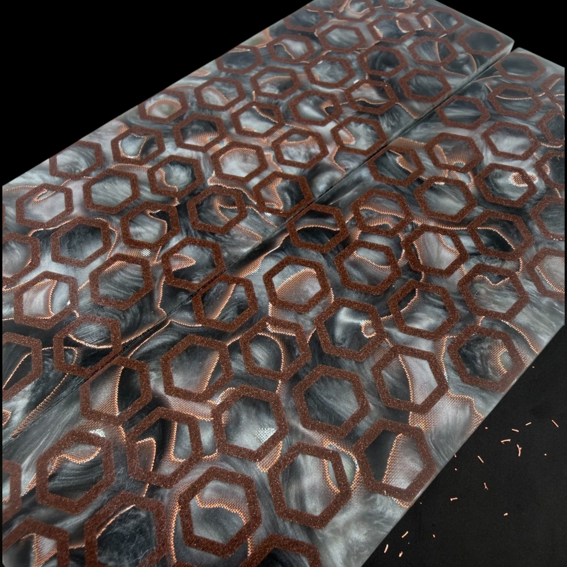 A close-up of a rectangular panel with a raised honeycomb pattern outlined in copper over a marbled gray, black, and white surface, photographed on a black background. JHC CopperCore crater hex knife scales 
