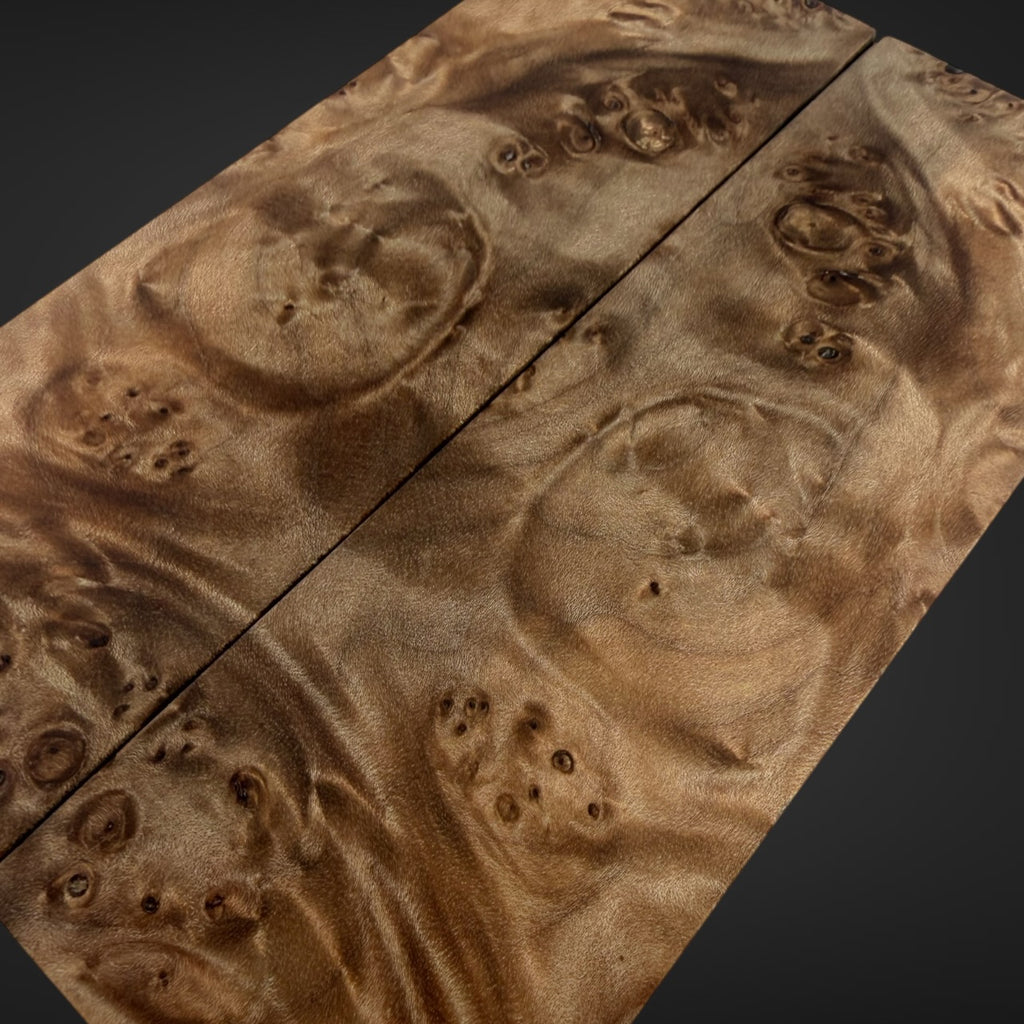 A close-up of a highly figured burl wood panel with dramatic wavy grain patterns in warm brown and tan tones, shown against a dark background.