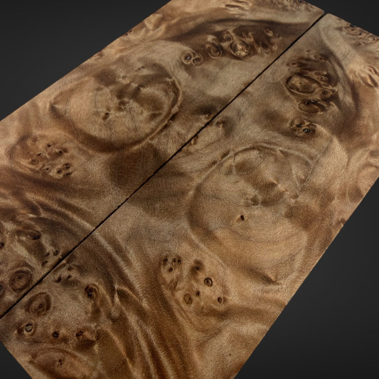 A close-up of a highly figured burl wood panel with dramatic wavy grain patterns in warm brown and tan tones, shown against a dark background.