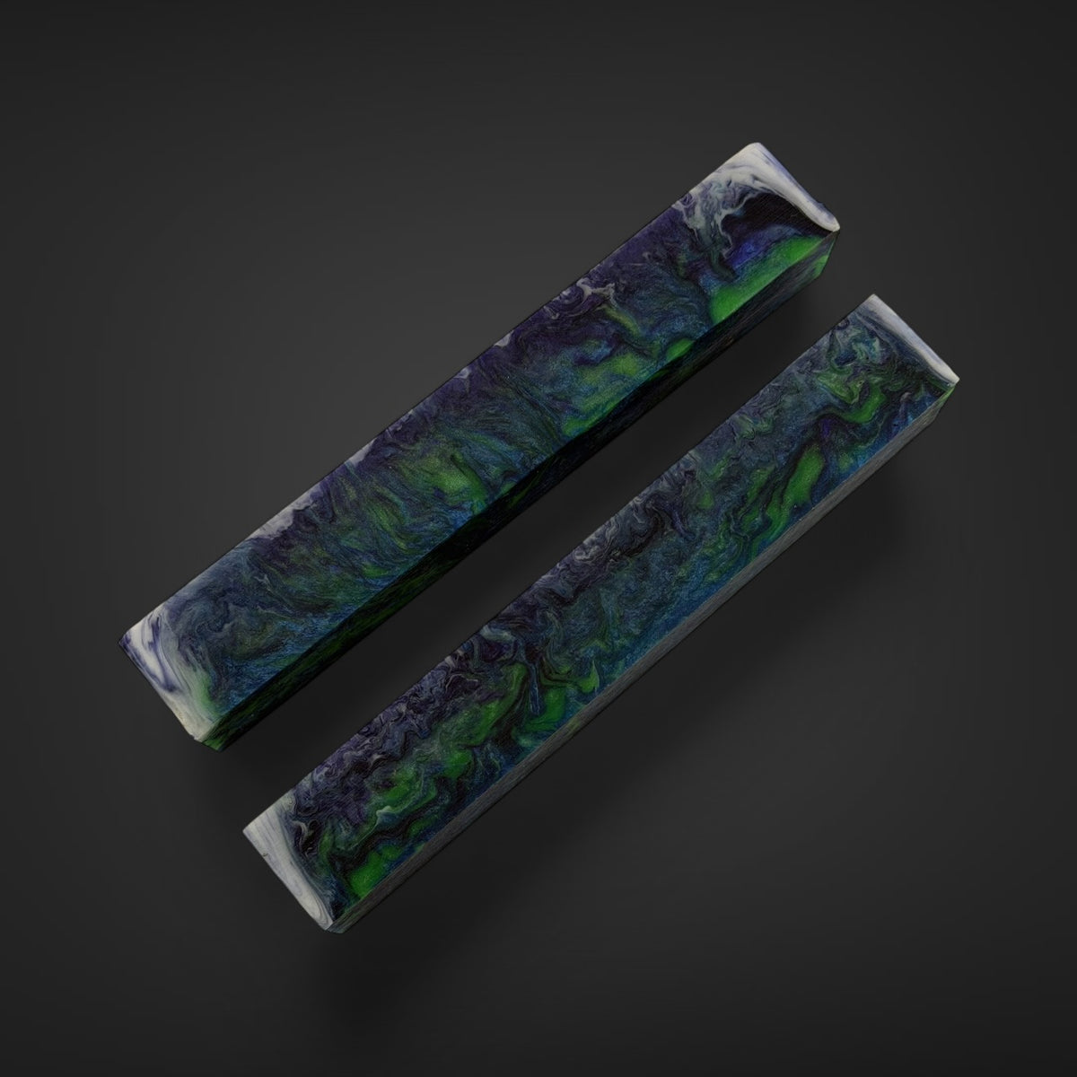 Wood turners material, lathe turners material . Resin pen and bead blanks Two rectangular resin strips with a marbled swirl pattern of green, blue, and black, displayed diagonally on a dark gray background.